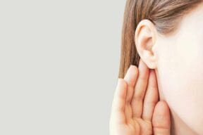 Woman listens attentively with her palm to her ear close-up on a gray background.